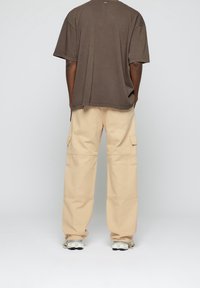 Brun bomull oversized t-shirt, beige cargobyxor med fickor, och vita sneakers. Enkel design, avslappnad passform, inga synliga mönster eller detaljer.
