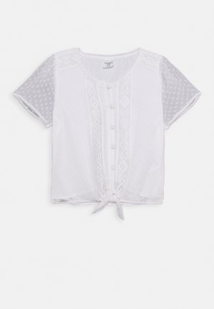 Blouse blanche avec manches courtes transparentes à pois, fermeture boutonnée à l'avant, accents brodés, et nœud noué à la taille.