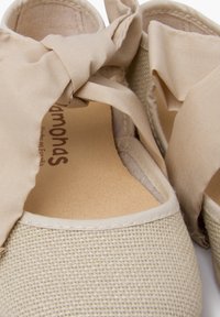 Espadrillas in tela beige con un corpo testurizzato, caratterizzate da un accento di tessuto annodato nella parte superiore e una soletta liscia di colore chiaro.