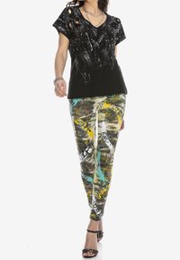 Camiseta negra desgastada con escote en V y salpicaduras de pintura, combinada con leggings de patrón de graffiti coloridos que presentan acentos de texto. Sandalias negras.