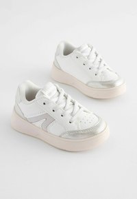 Baskets blanches avec des accents argentés, lacets texturés et bout perforé. Matériau synthétique doux, design low-top et semelle rembourrée.