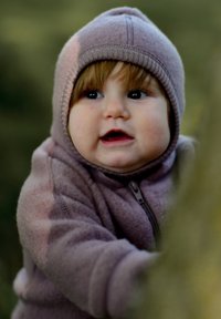 Hanorac cu fermoar din polar mov, cu glugă și manșete rib, purtat de un copil cu păr șaten deschis, zâmbind și ținându-se de un copac.