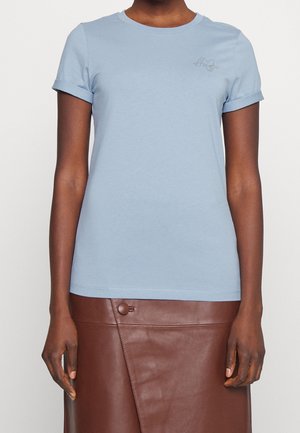 Personne portant un t-shirt bleu clair à manches courtes avec des revers roulés et une jupe en cuir marron avec un détail bouton.