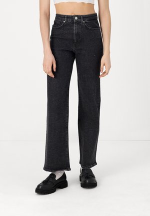 High-waisted black denim jeans with a straight-leg fit, subtle silver embellishments, and a raw hem. Worn with black shoes and white socks.
