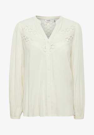 Fehér, hosszú ujjú blúz V-nyakkal, gombzárral és textúrált anyaggal, csipke részletekkel a mellkas és a vállak körül.