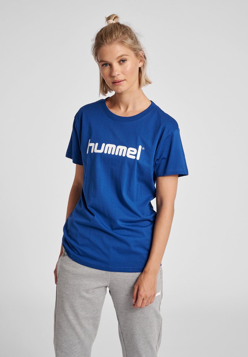 Blå bomullströja med rund halsringning och korta ärmar, prydd med en stor vit "hummel"-logga över bröstet. Grå sweatpants.