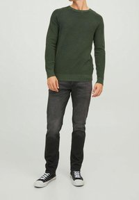 Grüner Strickpullover mit Rippstruktur, rundem Kragen und langen Ärmeln, kombiniert mit dunklen Jeans und schwarzen Sneakers.