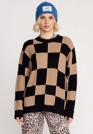 Dikke gebreide trui met afwisselend beige en zwarte blokken. Ribbelstructuur, ronde halslijn en lange mouwen. Gdragen met gebloemde broek.