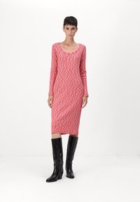 Rotes und weißes gemustertes Langarmkleid mit Rundhalsausschnitt, figurbetonter Silhouette und Länge bis zur Mitte der Wade, kombiniert mit knielangen schwarzen Stiefeln.