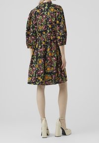 Černé květinové šaty s nadýchanými rukávy, zdobené barevnými květinami a s úzkým pasem. Vytvořené s béžovými lodičkami na vysokém podpatku.