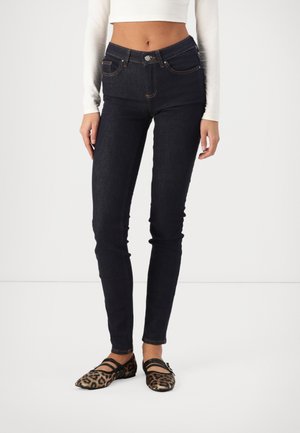 Tumedatest sinised kitsad teksad kõrge vöökohaga, millel on viis taskut ja kontrastne õmblus, koos leopardimustriliste korteritega.