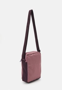 Borsa a tracolla quadrata con corpo rosa e accenti viola scuro, realizzata in tessuto resistente con superficie texturizzata e tracolla regolabile.