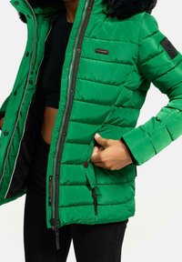 Chaqueta verde acolchada con cierre de cremallera, capucha de piel sintética negra y bolsillos laterales. Presenta una textura elegante y suave con un patrón acolchado.