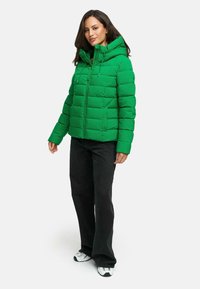 Grön pufferväst med huva, quiltat mönster, dragkedja fram och snörning, kombinerad med svarta vida byxor och sneakers.