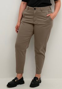 Beige tætsiddende bukser med en glat tekstur, tætsiddende form og sidelommer. Kombineret med sorte loafers med guldfarvede hardware-detaljer.