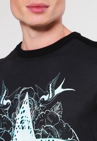 Black sweatshirt with a crew neck and contrasting ribbed collar. Features a blue graphic of birds and a star on the front. Cotton fabric.