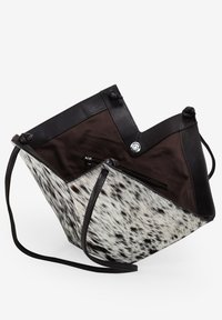 Bolso de piel y piel sintética con forma puntiaguda, que presenta un patrón de manchas en blanco y negro, correa delgada para el hombro y bolsillo con cremallera en el interior.