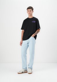 Black oversized t-shirt with a purple logo, light blue jeans, and light sneakers. Includes short sleeves, relaxed fit, and subtle texture.