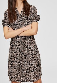 Svart blommig klänning med korta puffärmar, kragdecollté och figursydd midja. Har ljusfärgade blommönster över hela klänningen.