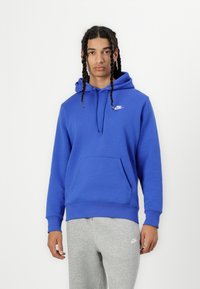 Sweatshirt azul com capuz e bolso frontal, apresentando um logotipo branco da Nike no peito. Combinado com calças de moletom cinzas.