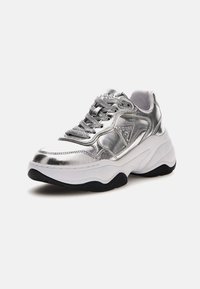 Zilveren metallic sneakers hebben een ronde neus, een witte zool met zwarte accenten en gestructureerde veters. De zijkant toont een logo-detail.