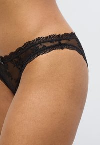 Musta pitsialushousut, joissa on kukkakuviot ja aaltoileva pitsireunus, esillä on läpikuultava, kevyt kangas pehmeällä tekstuurilla.