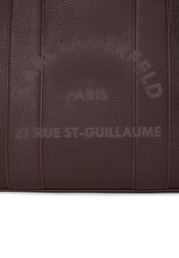 Mørkebrun teksturert læroverflate med "KARL LAGERFELD PARIS 21 RUE ST-GUILLAUME" preget med matchende mørkebrune bokstaver.