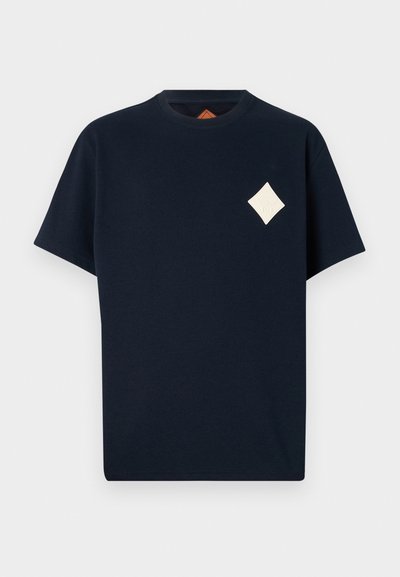Navy blue cotton t-shirt with a crew neck, short sleeves, and a cream diamond patch on the chest featuring embossed details.