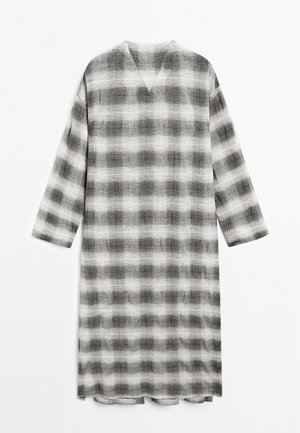 Lang, løstsiddende kjole med V-udskæring, der har et sort-hvidt ternet mønster. Lavet af tekstureret stof med trekvartærmer.