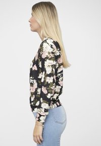 Top floreale a maniche lunghe di colore nero con fiori rosa e bianchi, caratterizzato da un orlo arrotondato e polsini arricciati. Indossato con jeans azzurri chiari.