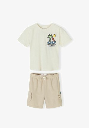 T-shirt à manches courtes crème avec motif graphique de palmier, vagues, planche de surf et soleil, accompagné d'un short beige à taille élastique avec poches latérales.