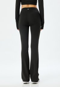 Leggings acampanados negros hechos de un material elástico, con una cinturilla alta y una textura suave, que presentan un pequeño logo en la parte trasera.