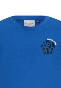 Niebieska bawełniana koszulka z okrągłym czarnym nadrukiem z napisem "RETOUR JEANS" oraz okrągłym wzorem na klatce piersiowej. Okrągły dekolt i krótkie rękawy.