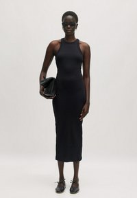 Schwarzes, figurbetontes, geripptes Midikleid mit hohem Hals. Kombiniert mit einer schwarzen Clutch und flachen schwarzen Schuhen, die eine elegante Silhouette schaffen.