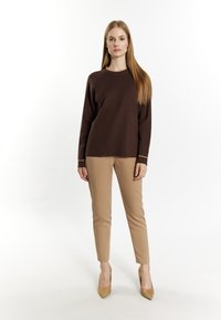 BraunerStrickpullover mit Rundhalsausschnitt, kombiniert mit beigen, schmal geschnittenen Hosen und hautfarbenen High Heels. Glatte Textur, schlichtes Design.