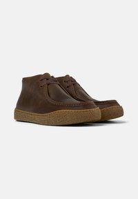 Pair of brown leather ankle boots with thick textured rubber soles and lace-up fronts on plain white background.