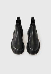 Pair of black leather Chelsea boots with pull tabs and chunky black soles, viewed from the front on a white background.