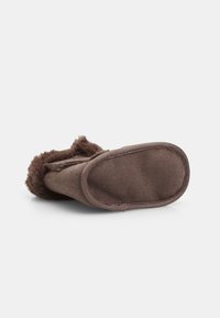 Brunt toffel med en mjuk, strukturerad yta och pälsdetalj; platt gummisula med sömmar längs kanten.