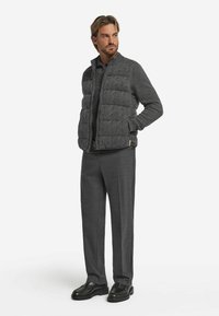 Graue gesteppte Weste mit strukturiertem Rautenmuster über einem passenden Pullover, kombiniert mit maßgeschneiderten grauen Hosen und dunklen Schuhen. Einfaches, modernes Design.