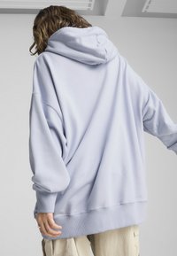 Sweat à capuche oversize bleu clair avec cordon de serrage, poignets côtelés et texture douce, offrant une coupe décontractée et des épaules tombantes.