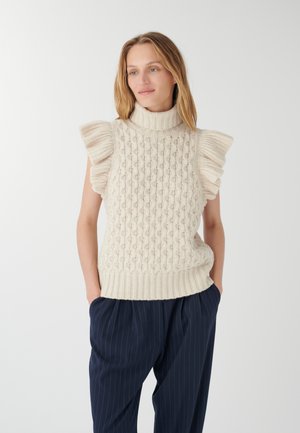 Cremfarbener, gestrickter ärmelloser Rollkragenpullover mit puffigen Schultern, strukturiertem Muster und geripptem Saum. Kombiniert mit dunklen, gestreiften Hosen.