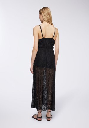 Abito max lungo in pizzo nero con spalline sottili, vita elastica e tessuto trasparente. Presenta motivi di pizzo intricati e una silhouette fluida.