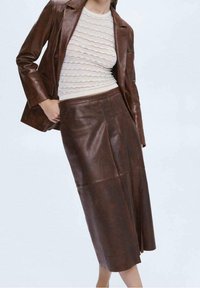 Bruine leren rok met een slank ontwerp, met een getailleerde taille en een rechte silhouet. Getextureerde gebreide top in een lichte kleur eronder.