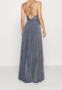Lång plisserad klänning i ett glittrande silver- och blått tyg. Har korsade axelband och en öppen ryggdesign.