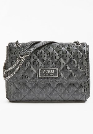 Sac à main matelassé noir Guess avec bandoulière chaîne et plaque logo métallique indiquant "GUESS EST 1981" sur le rabat avant.