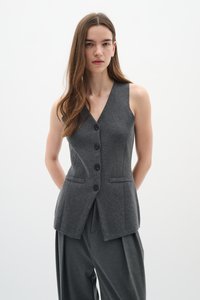 Gilet grigio senza maniche in misto lana, con scollatura a V profonda, cinque bottoni neri e due tasche frontali, abbinato a pantaloni grigi a gamba larga.