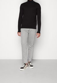 Musta pitkähihainen pooloneule, harmaat suorat farkut ja tennarit, joissa on mustia, beigejä ja valkoisia yksityiskohtia. Sileä pinta, vartalonmyötäinen malli.