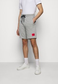 Shorts en sweat gris avec une taille élastique et un cordon noir. Comprend des poches latérales et un patch logo rouge sur la cuisse gauche.