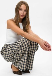 Pantalon large à carreaux en marine et crème, avec une coupe décontractée et des poches latérales ; associé à un débardeur côtelé blanc et des talons marron.
