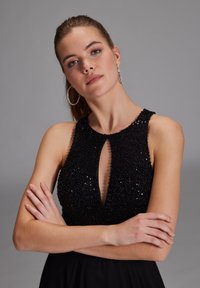 Schwarzes Abendkleid mit einem mit Perlen besetzten Oberteil und einem Ausschnitt in Schlüsselform. Der Rock fließt elegant und schafft eine geschmeidige Silhouette.